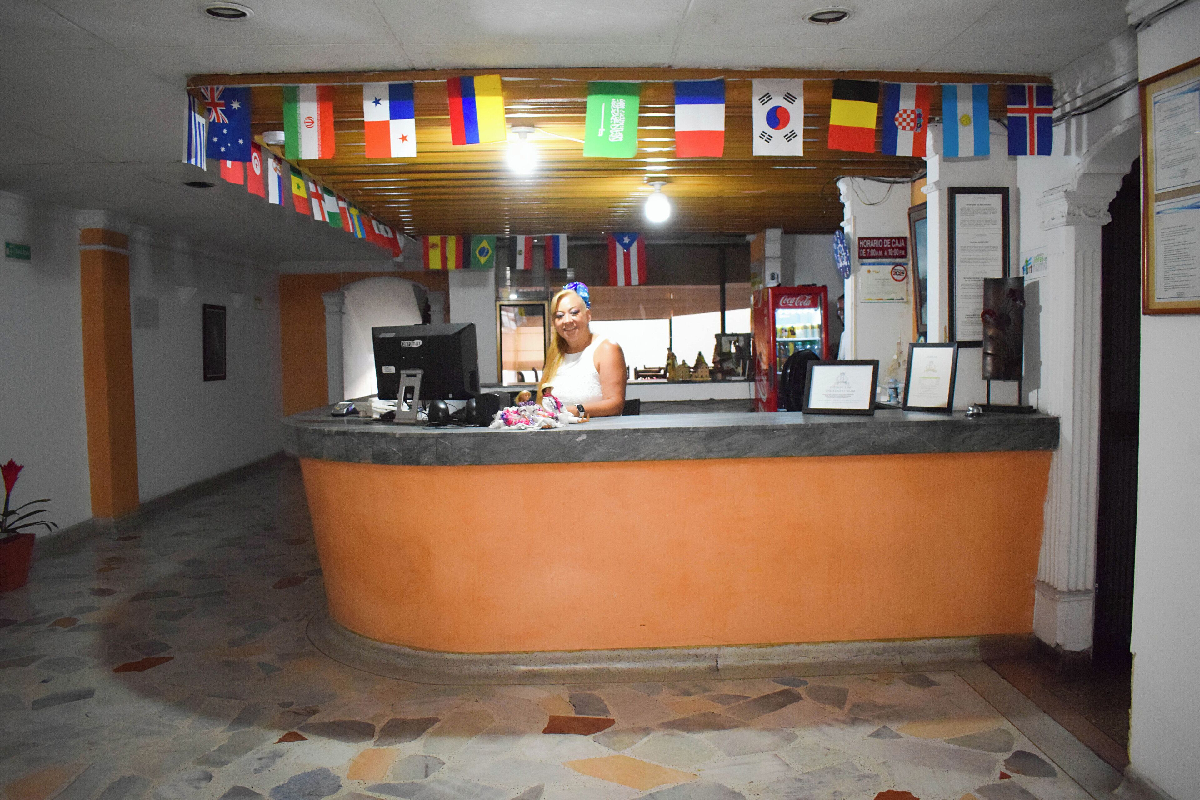 Un área de recepción con un mostrador curvo, una máquina de café y varias banderas colgadas.