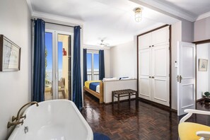 A hotel room with a large bathtub, a bed with a blue bedspread, a small table, and a wardrobe. - Villa Sea Shore Dio by Villa Plus (Gaula)