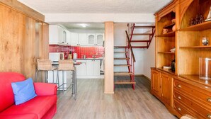 Ein gemütlicher Wohnraum mit Küchenzeile, einem roten Sofa, einem Holzschrank und einer Treppe zu einer oberen Ebene.