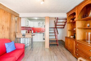 Ein kompakter Wohnbereich mit Küchenzeile, einem roten Sofa und einem Holzkabinett mit Dekoration.