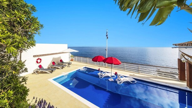 Ein Swimmingpool mit Liegestühlen und Sonnenschirmen, eine Flagge und Blick auf das Meer.