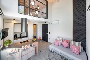 A modern kitchen with a central island, bar stools, a dining area with a sofa and cushions, and a large window with a view. - Villa Fire by Villa Plus (Kariotes)