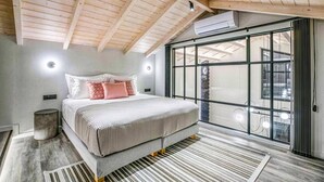 Una camera da letto con un letto, comodini, un'ampia finestra e un soffitto in legno.
