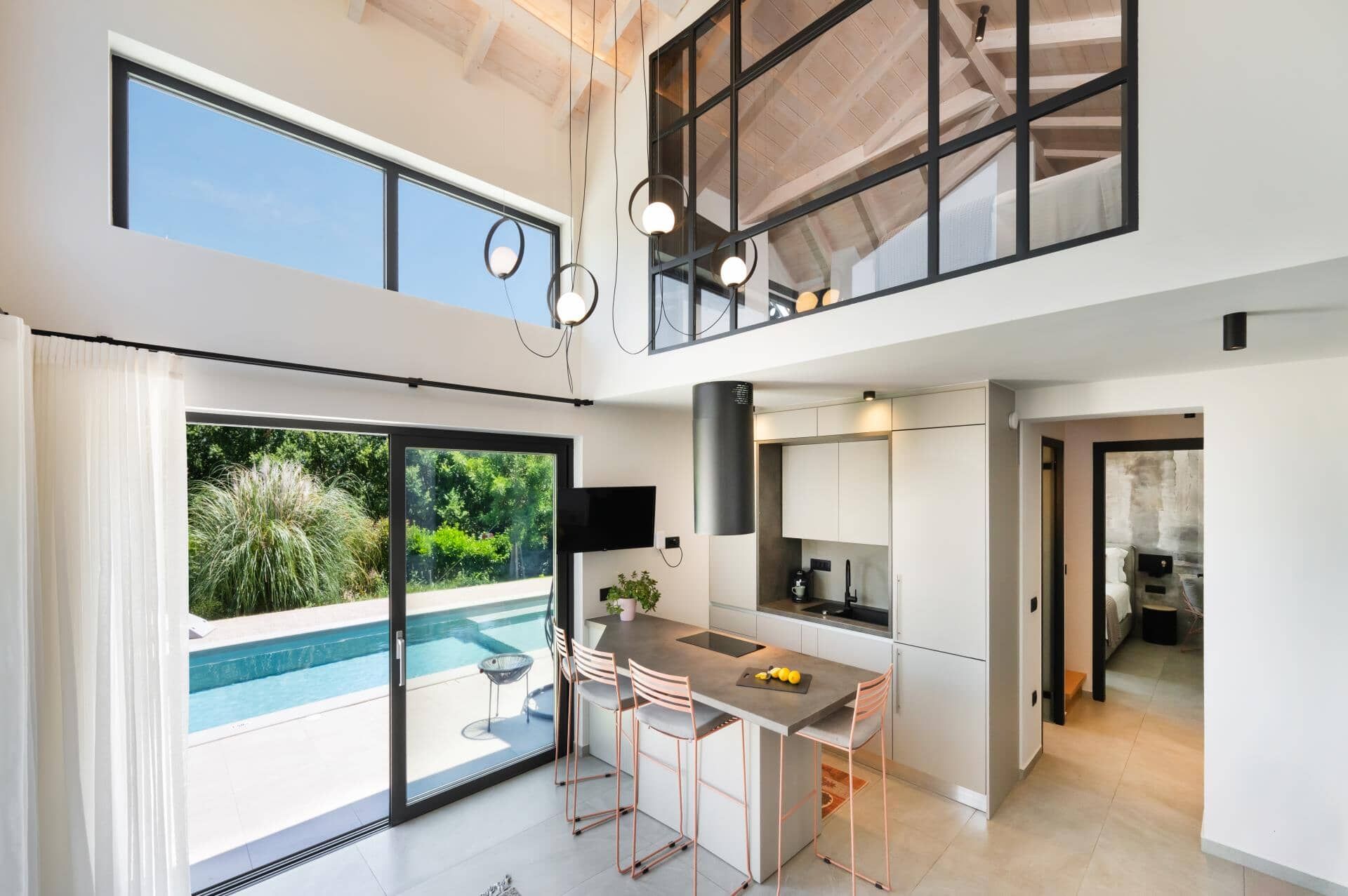 A modern kitchen with a central island, a dining area with chairs, and a large sliding glass door leading to a pool.