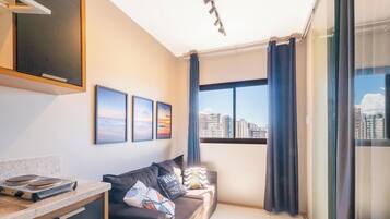A modern living room with a sofa, a flat-screen TV, and a city view through large windows.