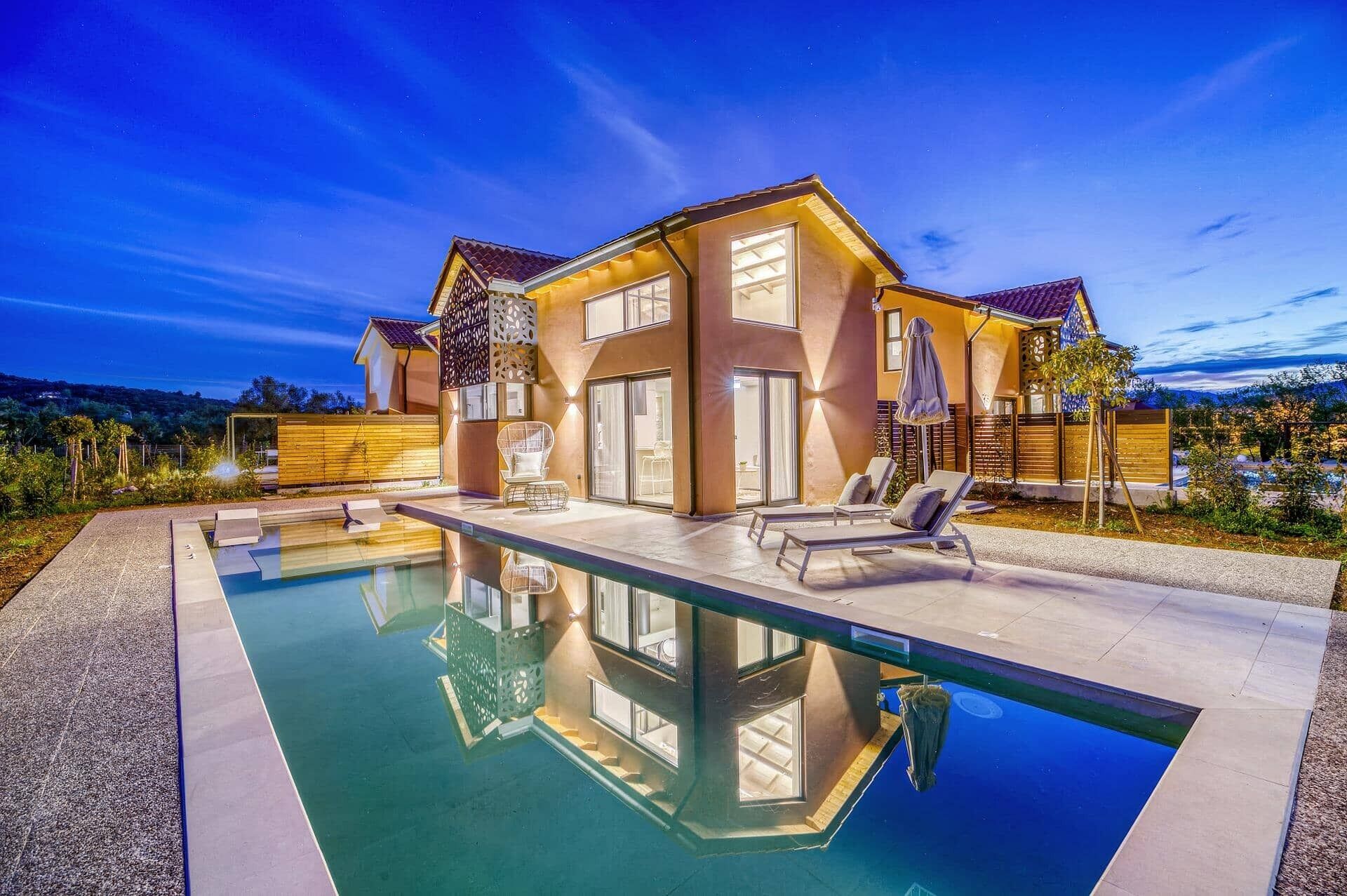 Una casa moderna con piscina, múltiples sillones de descanso y un jardín cuidado.