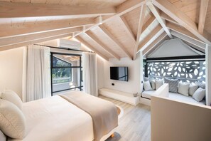 Ein modernes Schlafzimmer mit einem großen Bett, einer Sitzecke mit Kissen, einem Fernseher und einem Fenster mit Blick.