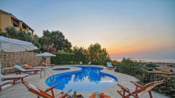 Un área de piscina con sillones de descanso, una mesa con bebidas y una pared de piedra.