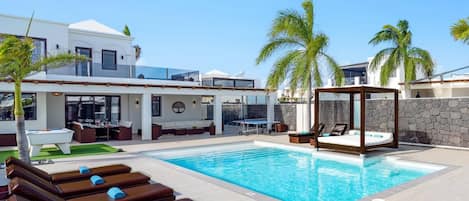 A pool area with lounge chairs, a table, and a canopy structure.