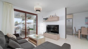 Ein modernes Wohnzimmer mit einer Couch, einem Couchtisch, einem Fernseher und einer Schiebetür zum Balkon.