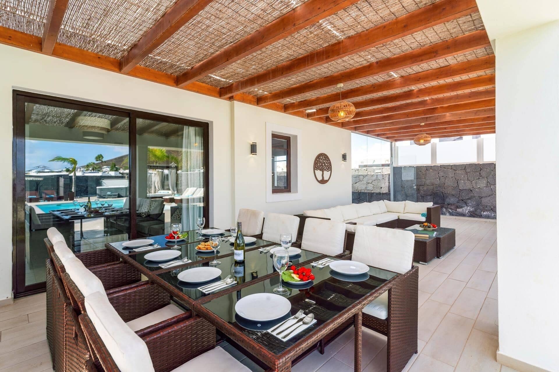Un coin repas avec une table en verre, des chaises en osier et une vue sur une piscine et des montagnes.