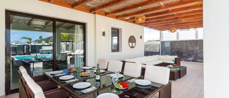 Un coin repas avec une table en verre, des chaises en osier et une vue sur une piscine et des montagnes.