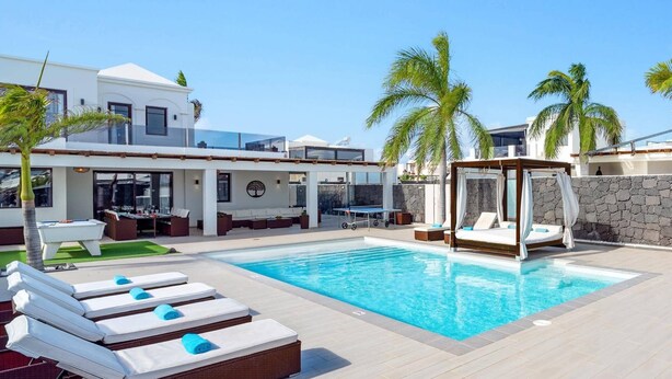 Ein Poolbereich mit Liegestühlen, einem Baldachinbett und einem modernen Gebäude mit großen Fenstern.