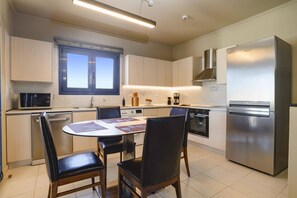 A modern kitchen with a central island, stainless steel appliances, and a dining area with chairs. - Villa Kalymnos by Villa Plus (Kolympia)