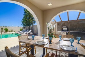 An outdoor dining area with a pool, lounge chairs, and an open kitchen. - Villa Kalymnos by Villa Plus (Kolympia)