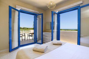 A bedroom with a bed, two pillows, a nightstand, a mirror, and a view of a terrace with a table and chairs. - Villa Kalymnos by Villa Plus (Kolympia)