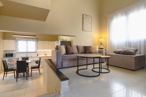 A modern living room with a sofa, a dining area with chairs, a kitchen in the background, and a large window with curtains. - Villa Kalymnos by Villa Plus (Kolympia)