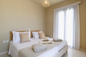 A hotel room with a bed, a headboard, a window with curtains, and a hanging light fixture. - Villa Kalymnos by Villa Plus (Kolympia)