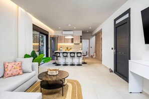 A modern living room with a sofa, a coffee table, and a kitchen area with bar stools. - Villa Terra Magna Alba by Villa Plus (Gennadi)