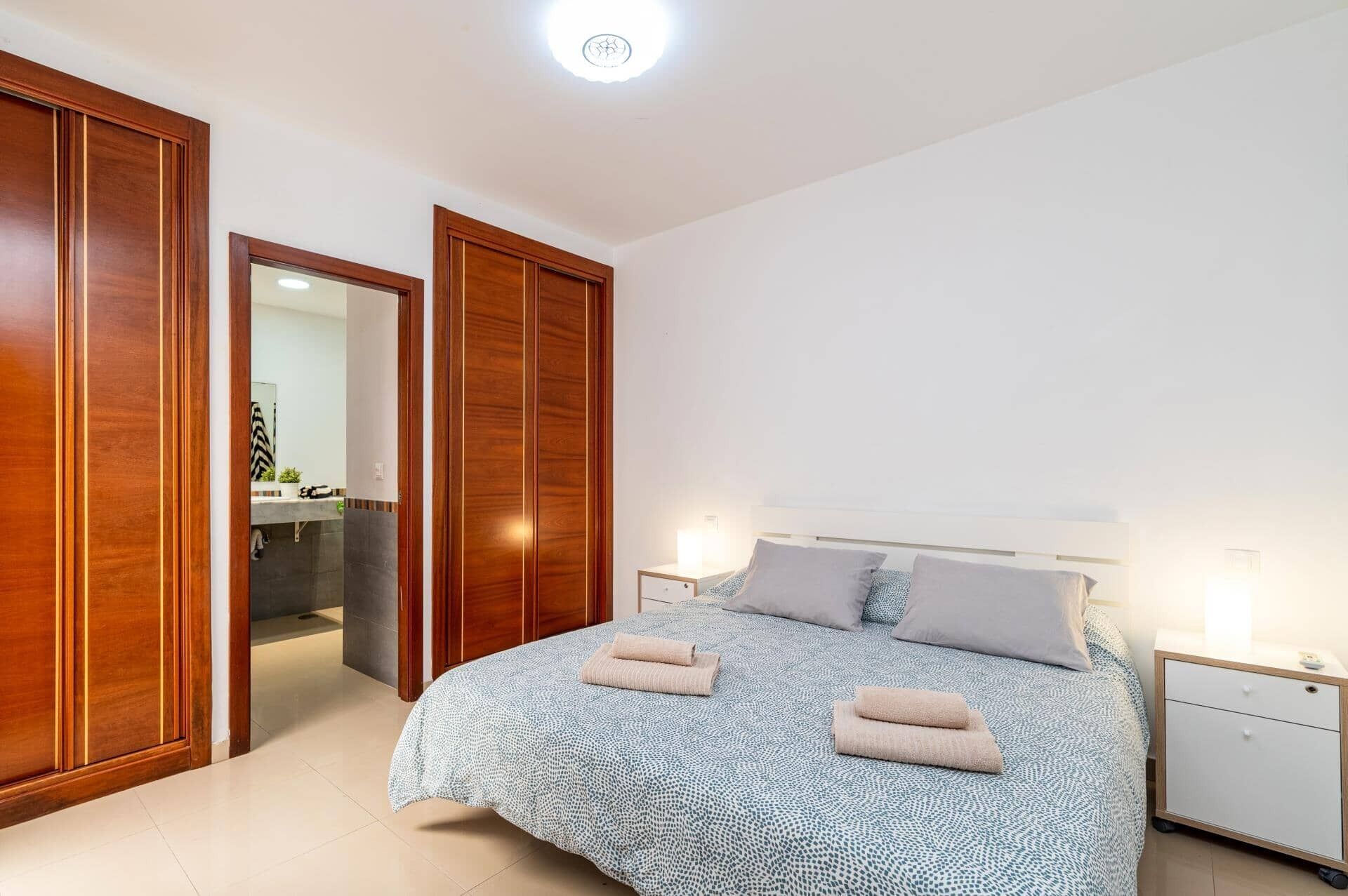 Een slaapkamer met een bed, twee nachtkastjes, een houten garderobe en een zichtbare badkamer door een geopende deur.