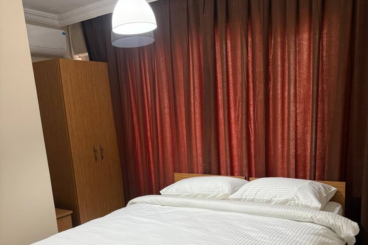 Una cama bien hecha con ropa blanca en una habitación con suelo de madera y un armario grande.