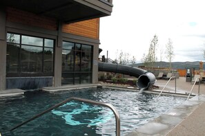 A swimming pool with a water slide, surrounded by a wooden deck and a building with large windows. - Ski-in/Ski-out Condo Week 1/25 to 2/1 International Snow Sculpture Championship (Breckenridge)