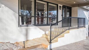 Un edificio moderno con fachada de ladrillo blanco, ventanas amplias y una escalera de madera con barandillas negras.