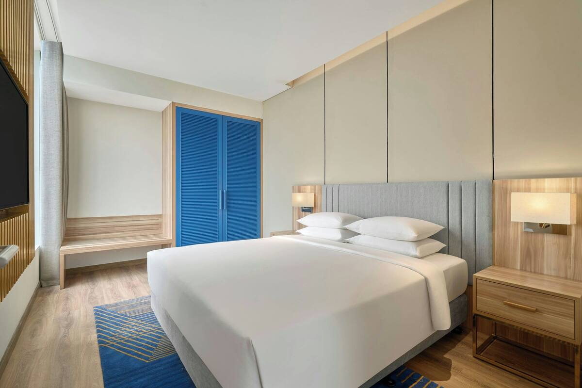 Une chambre d’hôtel avec un grand lit, une table de chevet avec une lampe, une armoire et un téléviseur.