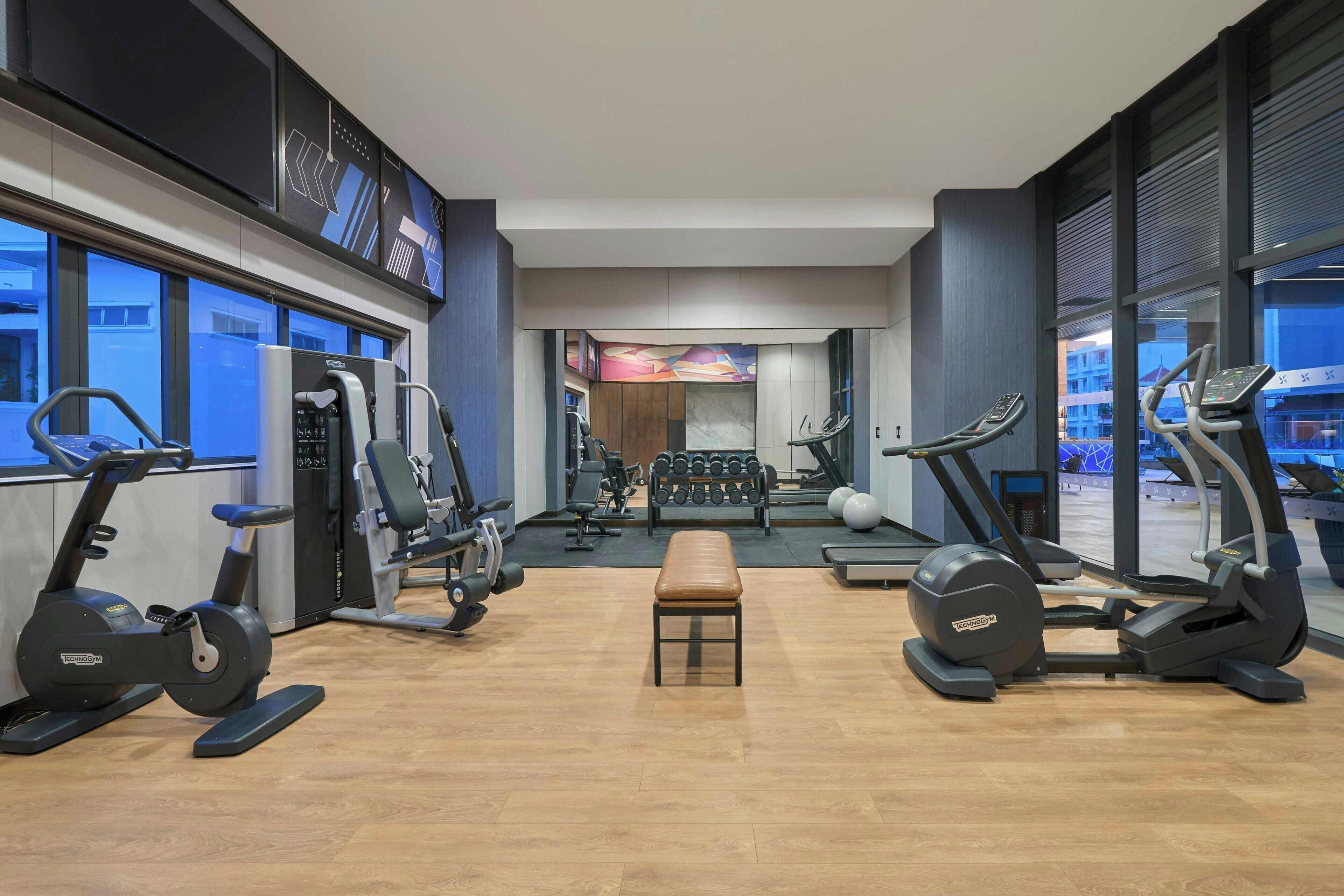 A modern gym with cardio equipment, weight machines, and a bench.