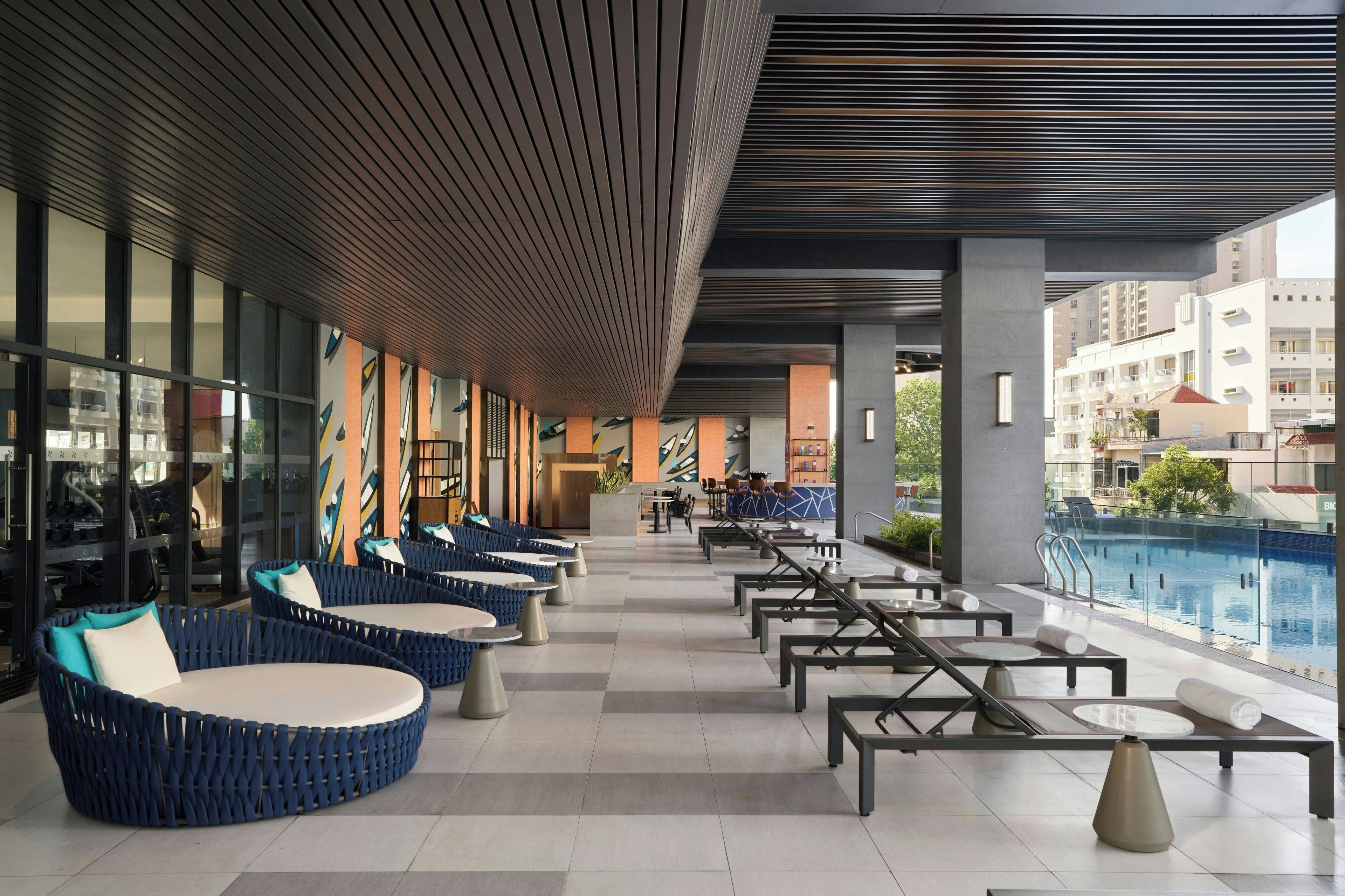 A modern outdoor seating area with round tables and blue cushioned chairs, overlooking a swimming pool.
