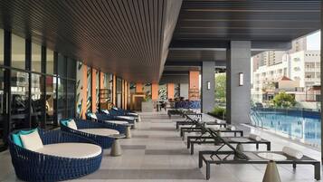 A modern outdoor seating area with round tables and blue cushioned chairs, overlooking a swimming pool.