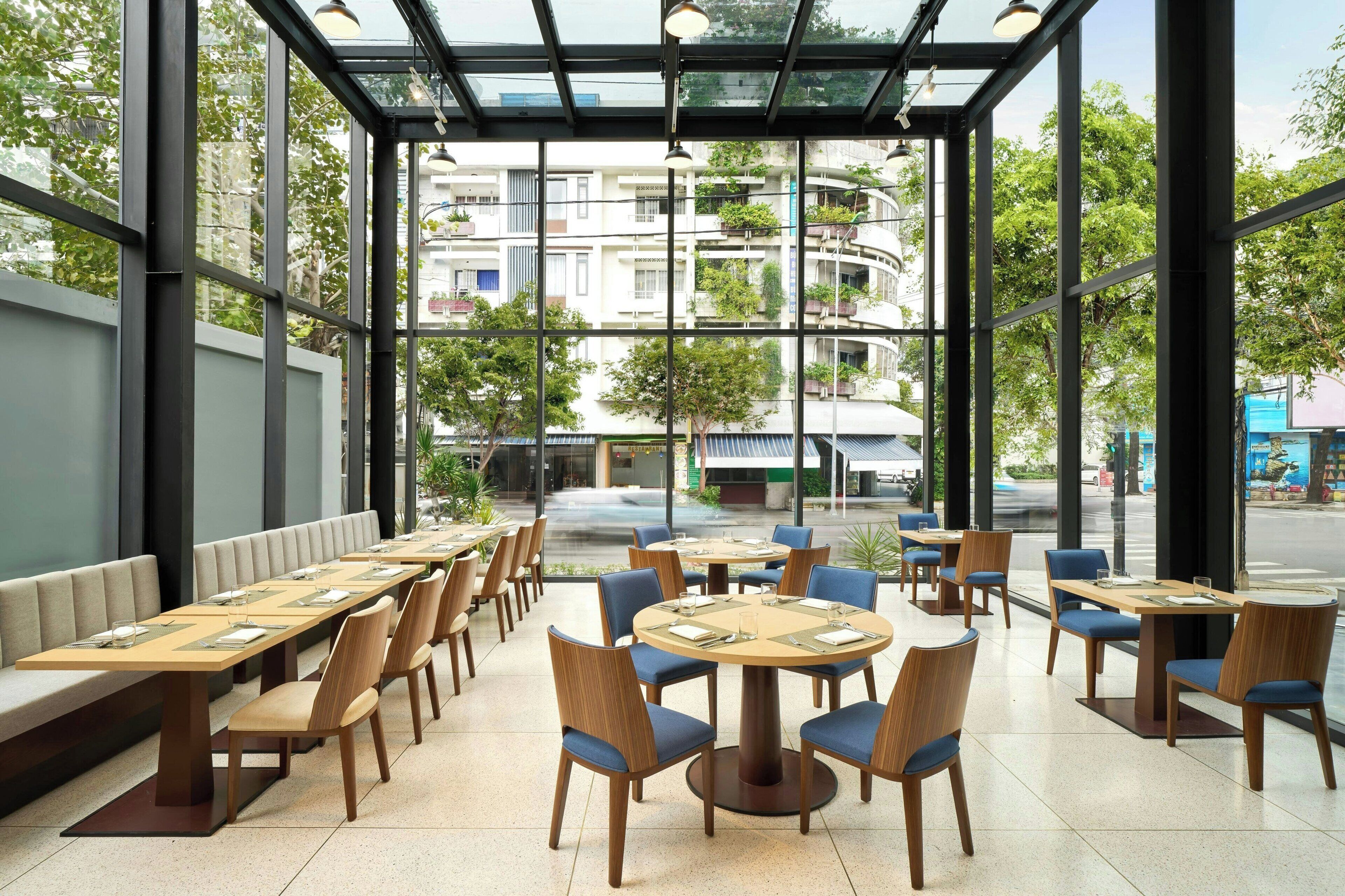 A modern restaurant with a glass-enclosed patio, wooden tables and chairs, and a view of the cityscape.