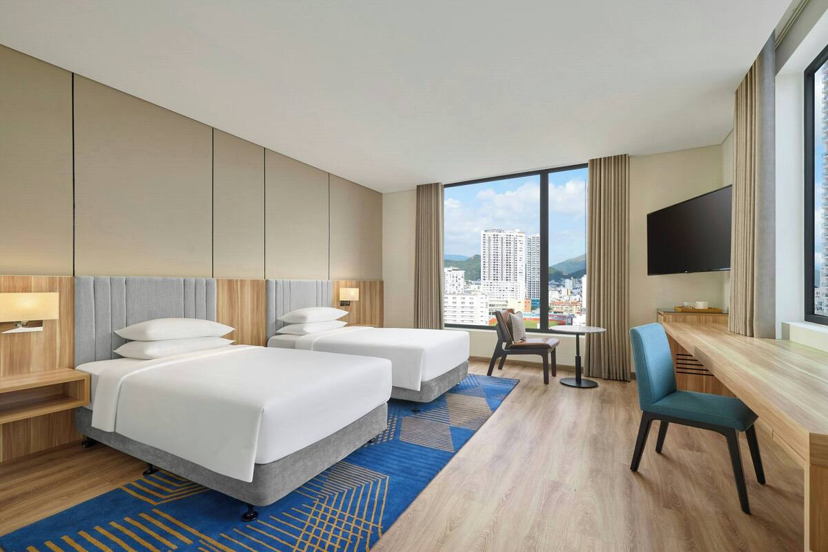 Une chambre d’hôtel avec deux lits, un bureau, une télévision et une vue sur la ville.