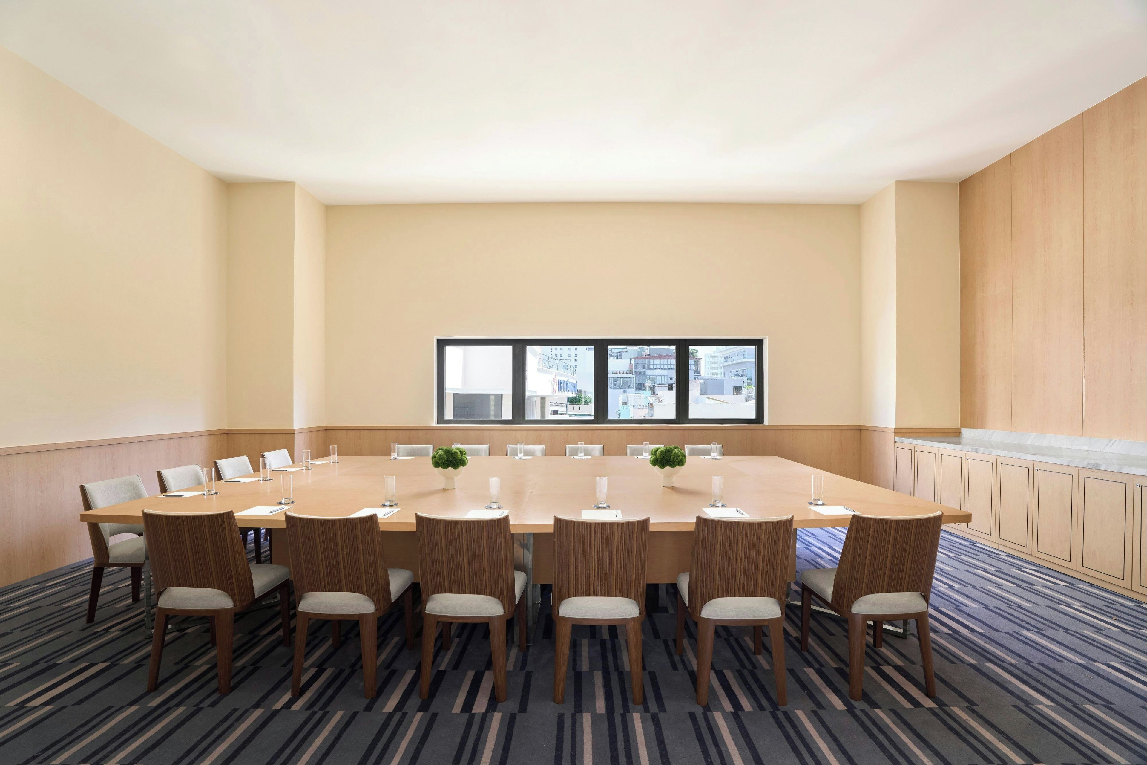A conference room with a large table, chairs, and a view of buildings through the windows.