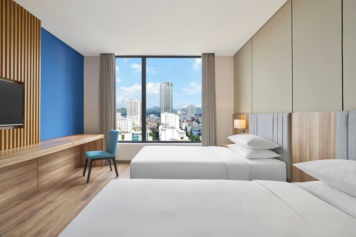 Une chambre d’hôtel avec vue sur la ville, un bureau, une chaise, deux lits et un téléviseur.