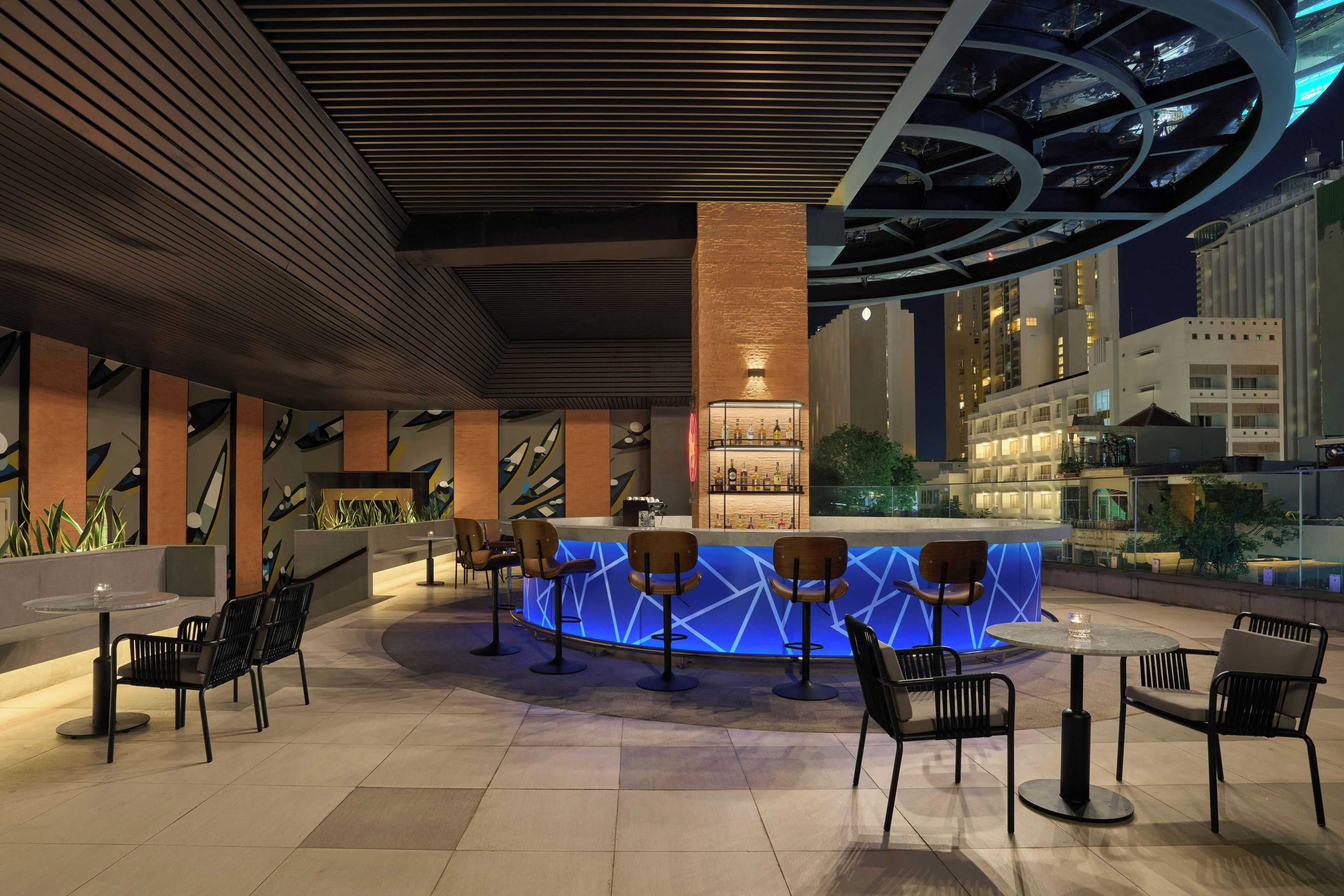 A modern bar area with a central counter, seating, and a view of the cityscape.