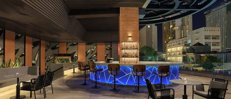 A modern bar area with a central counter, seating, and a view of the cityscape.