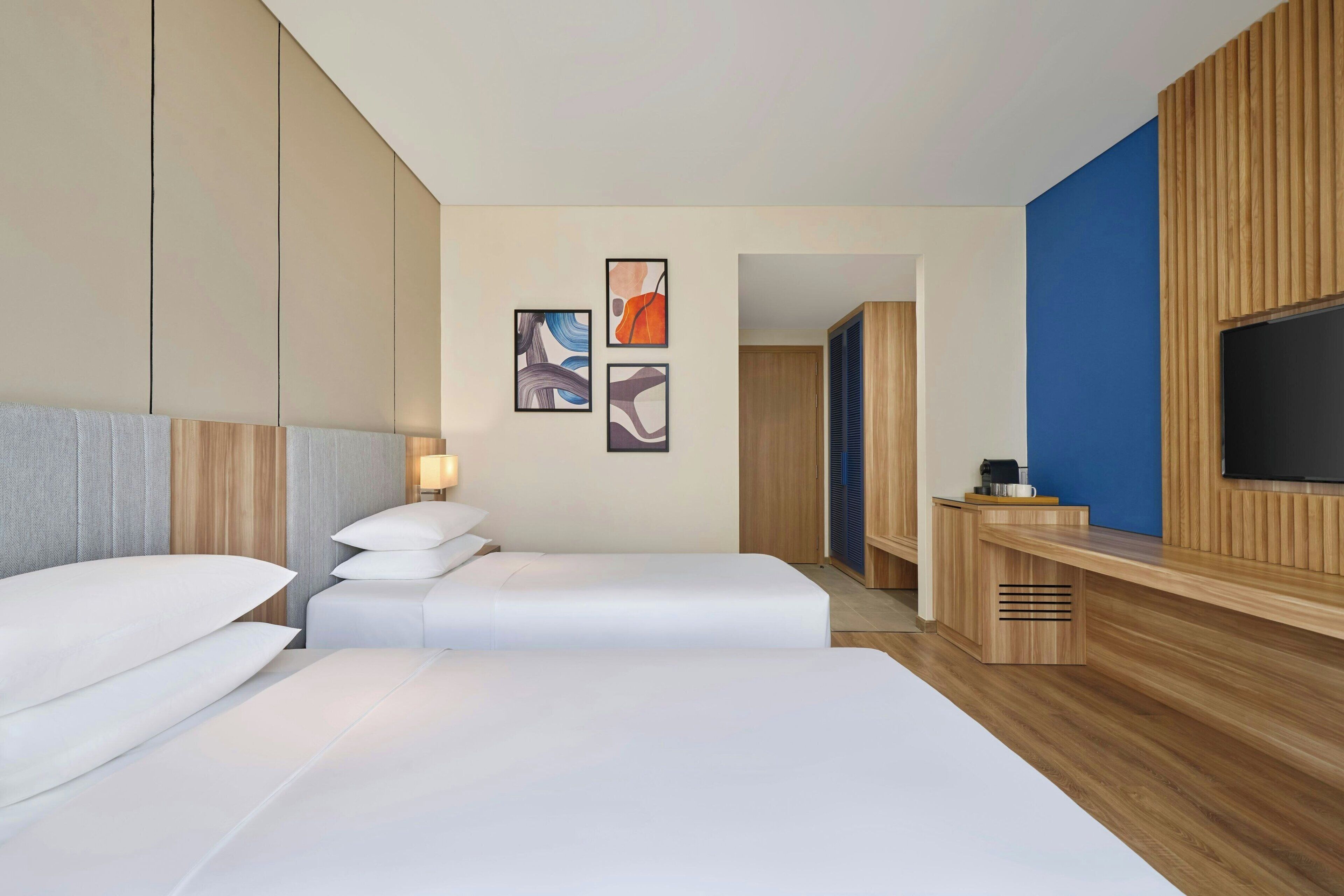 Een moderne hotelkamer met twee bedden, een televisie en kunst aan de muur.