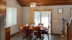 A dining area with a wooden ceiling, a ceiling fan, a dining table with chairs, and a window with blinds.