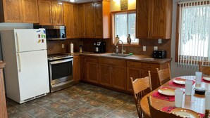 A kitchen with wooden cabinets, a refrigerator, a stove, a sink, and a dining table with chairs.