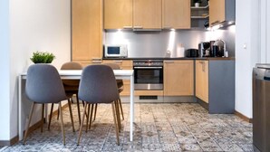 A modern kitchen with wooden cabinets, a microwave, stove, and a dining area with two chairs. - City center with Free parking and Sauna (Tallinn)