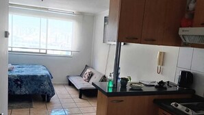 A compact kitchen with wooden cabinets, a built-in stove, and a small dining area with a bench. - Central apartment/studio family friends and couples (Santiago)