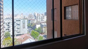 A view from a window with a metal grid, overlooking a cityscape with various buildings and a clear sky. - Central apartment/studio family friends and couples (Santiago)