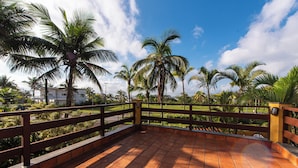 A terrace with a tiled floor, a wooden railing, and palm trees in the background. - Hotel Cia do Mar (Bertioga)