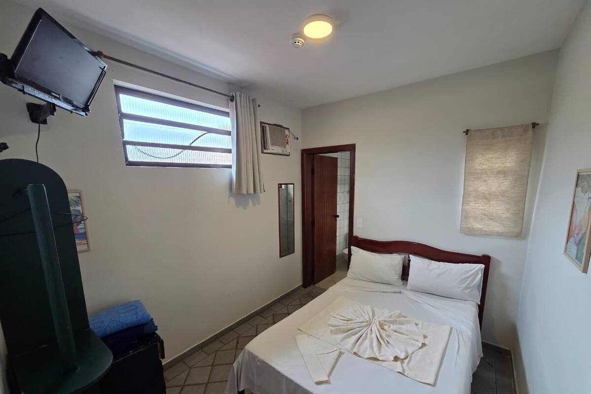 A hotel room with a bed, a television, a window with curtains, and a door.