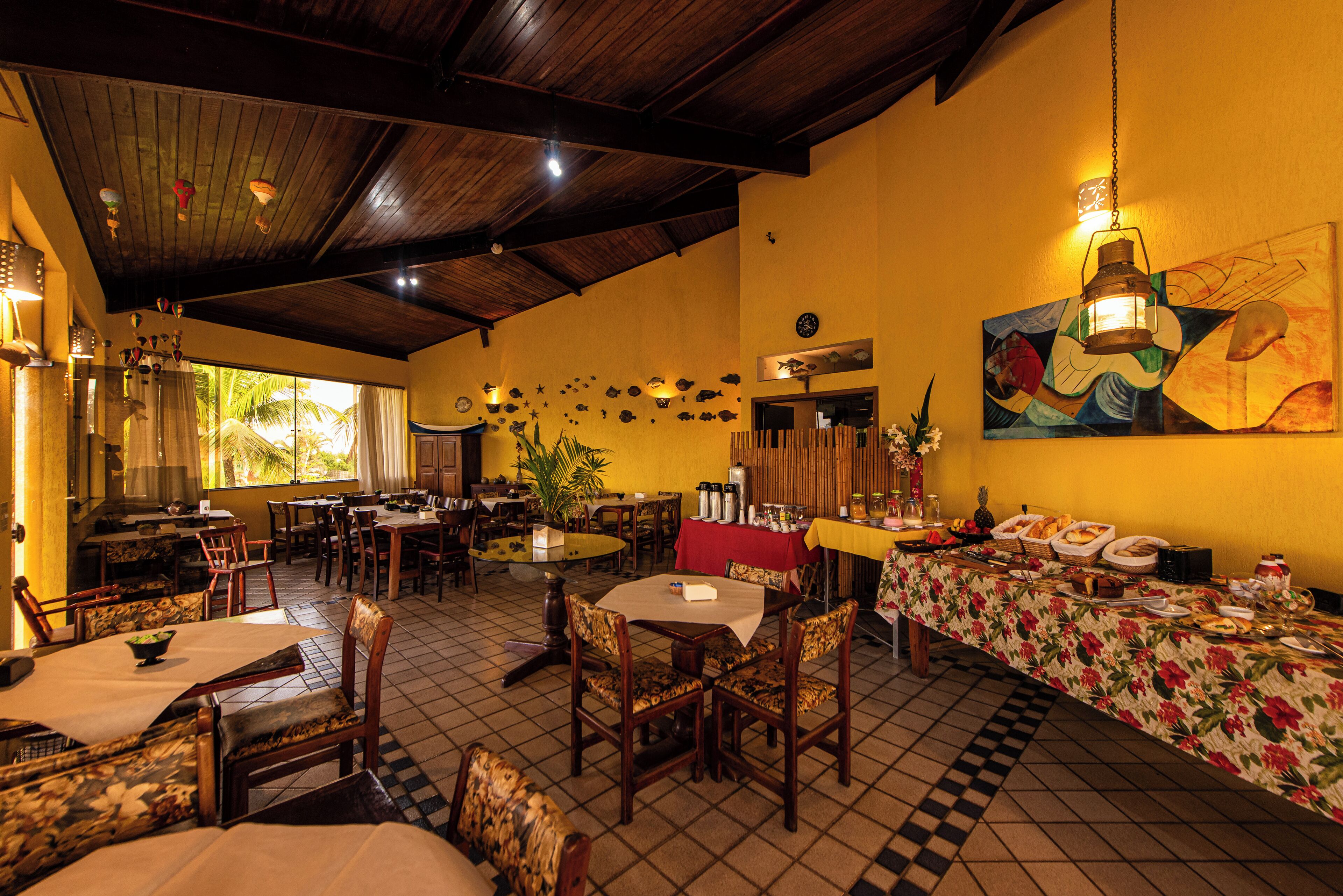 Restaurante com vigas de madeira no teto, piso de azulejos e mesa de buffet com diversos pratos.