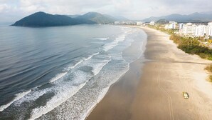 A beach with a sandy shore, waves, and a distant mountain. - Hotel Cia do Mar (Bertioga)