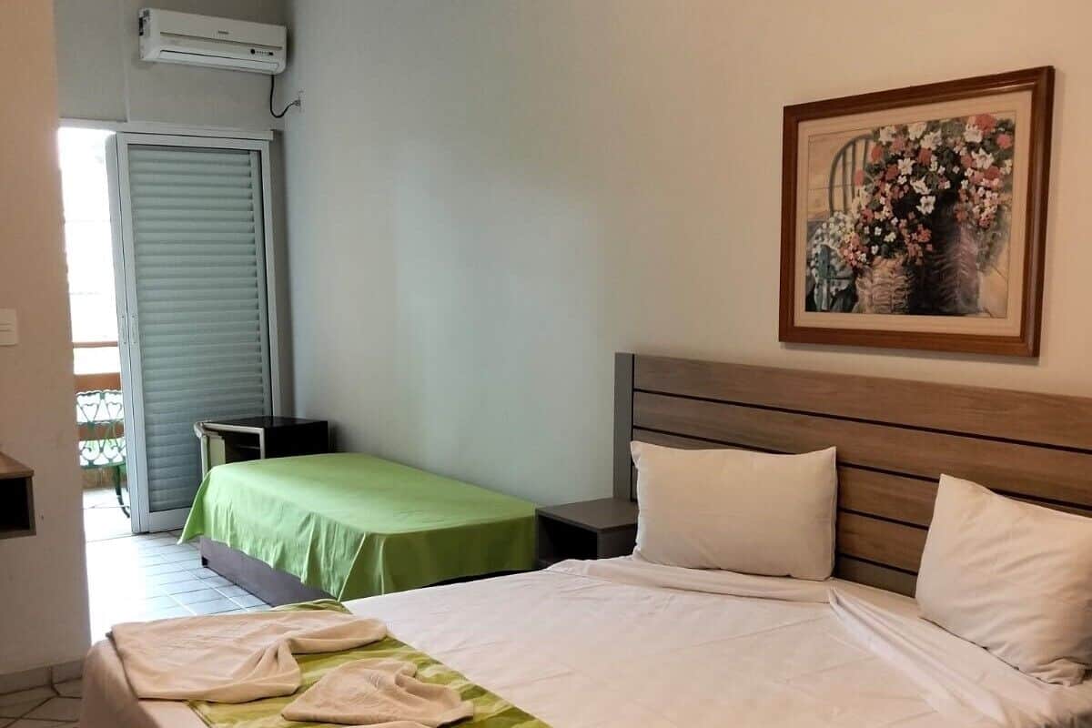 A hotel room with a bed, a smaller bed, a painting, and a sliding door.