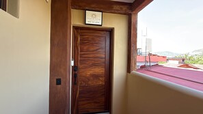 A wooden door with a sign above it, a balcony with a red floor, and a view of buildings and hills in the background. - Luxurious 2 bedroom condo Steps from Beach with ocean view from balcony. (Zihuatanejo)