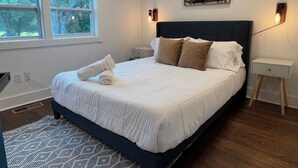 Un dormitorio moderno con una cama grande, un ventanal con persianas, una obra de arte en la pared y una mesita de noche con lámpara.